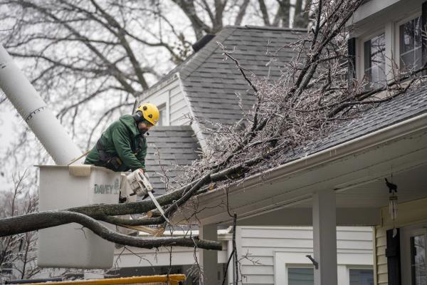 A crew from Davey Tree cuts a large tree branch back from a residential home and sidewalk on Woodward Heights in Pleasant Ridge, Mich., as ice causes widespread power outages in the metro Detroit area on Thursday, Feb. 23, 2023.