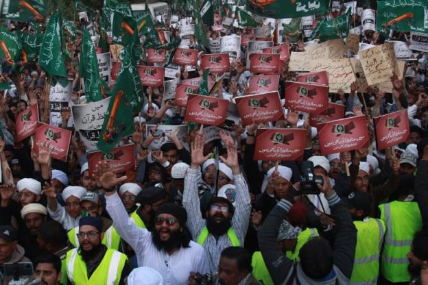 Protestors in Karachi, Pakistan, hold up signs and flags.