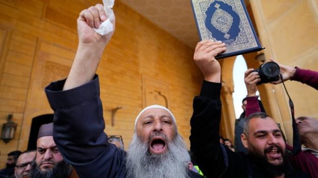 A man holds the Quran in the air, while another man shouts slogans during a protest in Beirut, Lebanon.