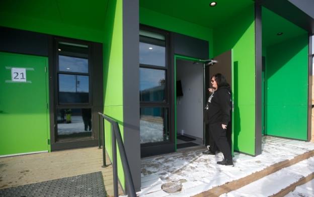 A woman stands in front of an open doorway next to a green wall 