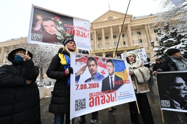People are shown in winter clothing holding posters in a rally outside a building.