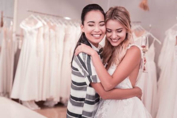 two women hugging in wedding gown and casual clothing at bridal shop